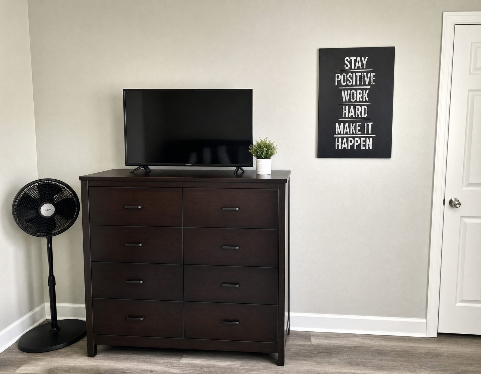 Bedroom dresser with a television, standing fan and a framed motivational print