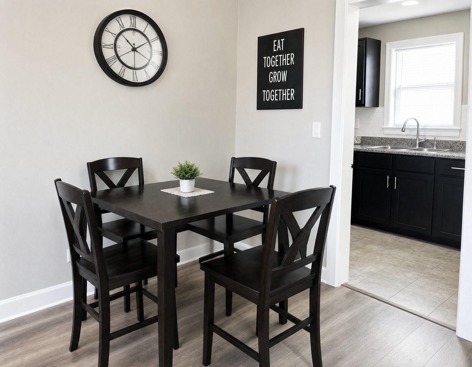 Dining area with a four-seat table and wall clock, opening into the kitchen